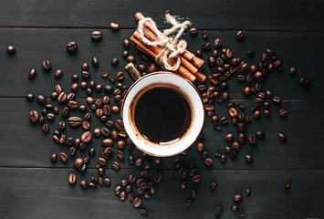 Cup of black coffee, coffee beans and cinnamon sticks on dark background