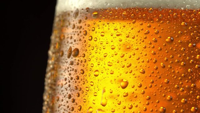 Glass of beer turns slowly around its axis. Close up 4K video. Black background.