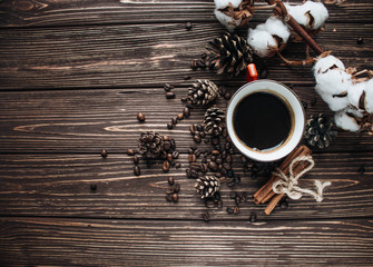 Close-up view of roasted coffee beans, cup of coffee, cotton flowers, cinnamon and pine cones