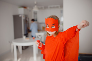 Child child is super hero in red suit standing in center of room at home. Concept power girl