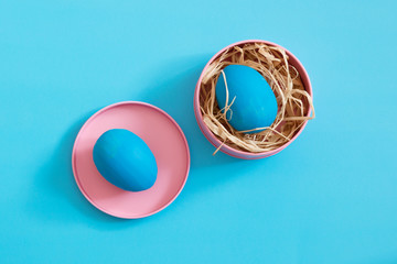 Two blue Easter eggs lie in brightly pink metal boxes. Blue background. Copy space.