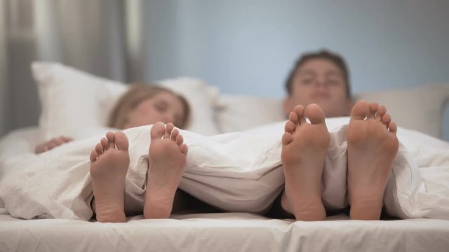 Young couple touching each other feet and toes, morning greeting, flirt in bed