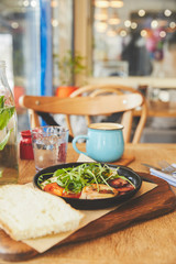 Hot breakfast dish of fried eggs in pan with coffee on table