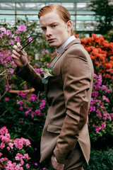 side view of stylish young man with red hair and eyeglasses in hand standing in glasshouse