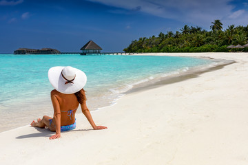 Fototapeta na wymiar Attraktive Frau mit weißem Sonnenhut liegt am tropischen Strand und genießt ihren Urlaub