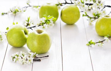 Ripe green apples with spring flowers on a white wooden background.