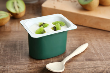 Plastic cup of yummy kiwi yogurt on wooden table