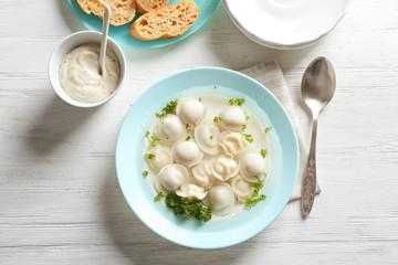 Tasty broth with dumplings on wooden table