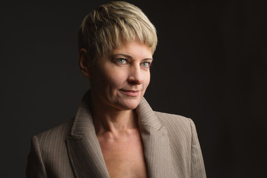 Beautiful Smiling 40 Year Old Woman. She Has A Short Hairstyle And She Wears A Jacket. Woman Isolated Over Black Background.