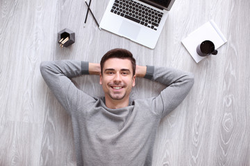 Young man with laptop lying on floor, top view