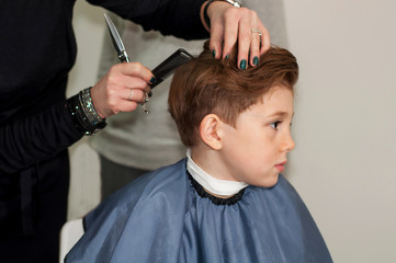 A handsome boy is made to styling the hands of a hairdresser