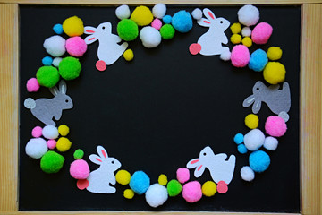 Oval multicolour frame from woolen Easter bunnies and eggs with copyspace for your text on the blackboard  background. Top view, flat lay