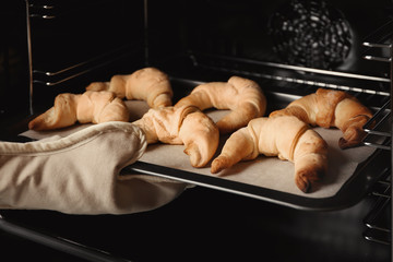 Person taking baking sheet with croissants from oven, closeup