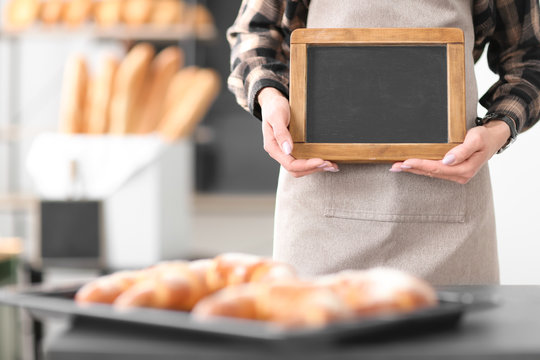Woman holding mini chalkboard in bakery. Small business owner