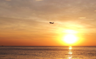 Silhouette of airplane flying over sea at the sunset