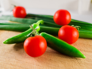 Little branch of cherry tomatoes, green onion leaves and hot peppers over wooden background.