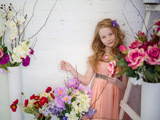 Beautiful girl 10 years old with red hair in the studio with flowers