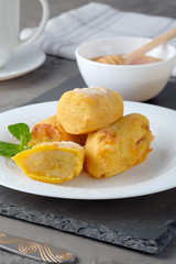 Bananas in batter and sprinkled with powdered sugar on a white plate on the gray slate background. Vertical view.