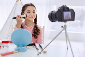 Best tutorial. Cheerful pre-teen girl explaining how to apply powder correctly while making a...
