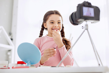 Lip care. Beautiful pre-teen girl with two braids filming a makeup tutorial and applying lip balm to her lips while filming it with a camera