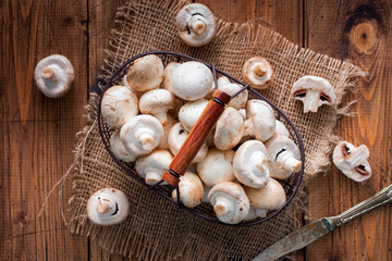 Raw fresh mushrooms in a metal basket on a wooden table, top view