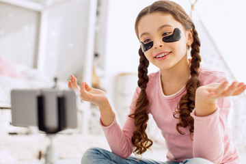 Informative vlog. Sweet pre-teen girl sitting cross-legged on the floor and reviewing under-eye...