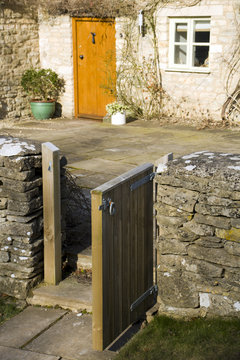 An Open Garden Gate Leading To A Stone Cottage Front Door