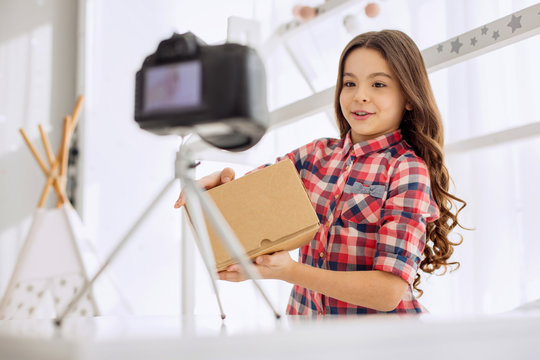 Introductory remarks. Pleasant cheerful pre-teen girl in a checked shirt holding a box in her hands and presenting it at the beginning in her unboxing video