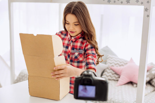 Curious child. Petite pre-teen girl in a checked shirt opening a box and looking inside curiously while recording a vlog