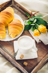 Coffee, croissant and flowers on bed