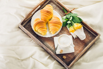 Coffee, croissant and flowers on bed top view
