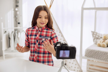 Pleasant interaction. Cheerful pre-teen girl recording a video blog and answering the questions of her audience in it while gesticulating