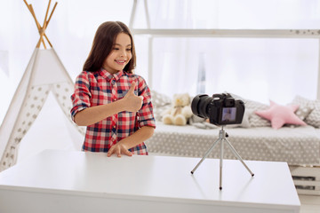 Best mood. Pretty pre-teen girl in a checked shirt filming a video blog and showing a thumbs up...