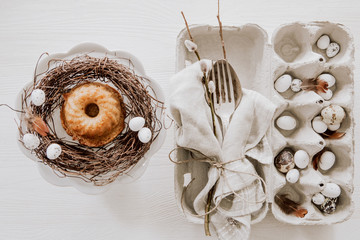 Natural Easter table decoration with silverware and cup cake in a wreath on white wooden table