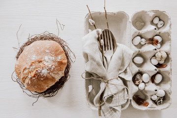 Natural Easter table decoration with silverware in egg box and homemade bread in a wreath on white wooden table