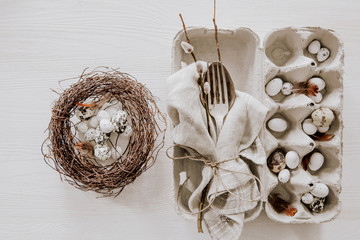 Natural Easter table decoration with silverware in egg box and eggs in a wreath on white wooden table
