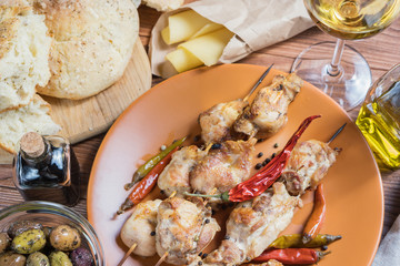 Grilled chicken meat, bowl with different kind of olives, glass of wine, cheese and fresh bread ciabatta on the wooden table.