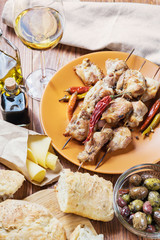 Grilled chicken meat, bowl with different kind of olives, glass of wine, cheese and fresh bread ciabatta on the wooden table.
