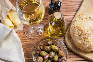 Bowl with different kind of olives, glass of wine, cheese and  fresh bread ciabatta on the wooden...