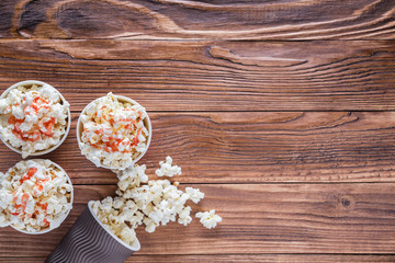 Obraz na płótnie Canvas Popcorn in paper cups on a rustic wooden background with copy space, top view, flat lay. Cinema concept. Sweet popcorn with strawberry syrup.