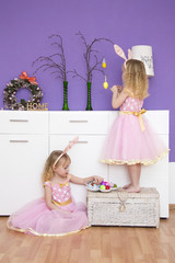 Easter holiday, little girls in beautiful pink dresses, girls help each other to decorate an apartment with decorative eggs