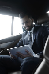businessman with a digital tablet sitting in the back seat of a car