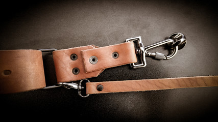 A beautiful brown hand made leather camera sling strap on a black background. Photographer equipment, stylish, vintage, retro feel. - Powered by Adobe