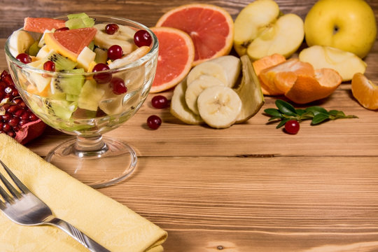 Diet fresh salad in a glass plate on a wooden background table with napkin and a fork on it next to citrus and fruits. Detox food ingredient concept