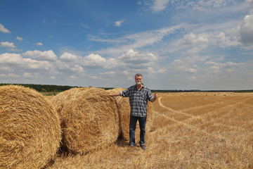 Naklejka na ściany i meble Farmer or agronomist in wheat field after harvest examining bale and gesturing with thumb up