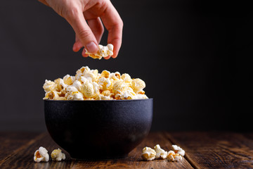 The hand takes popcorn from a stylish ceramic bowl.
