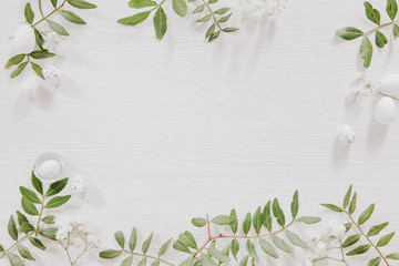 White and green Easter decoration with flowers, leaves and little eggs on white wood