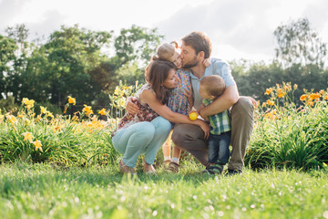 Fototapeta premium Young happy family having fun in flowers outdoors. Couple in love holding their cute children. Mother father daughter son.