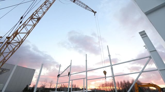 Industrial exterior, Mounting of metal structures against the background of an orange sky with clouds, construction work, construction of an industrial building, timelapse