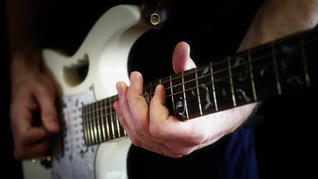 A musician plays solo on a white electric guitar on a black background. The man is playing rock.
